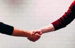 Handshake between two people against a white brick wall.